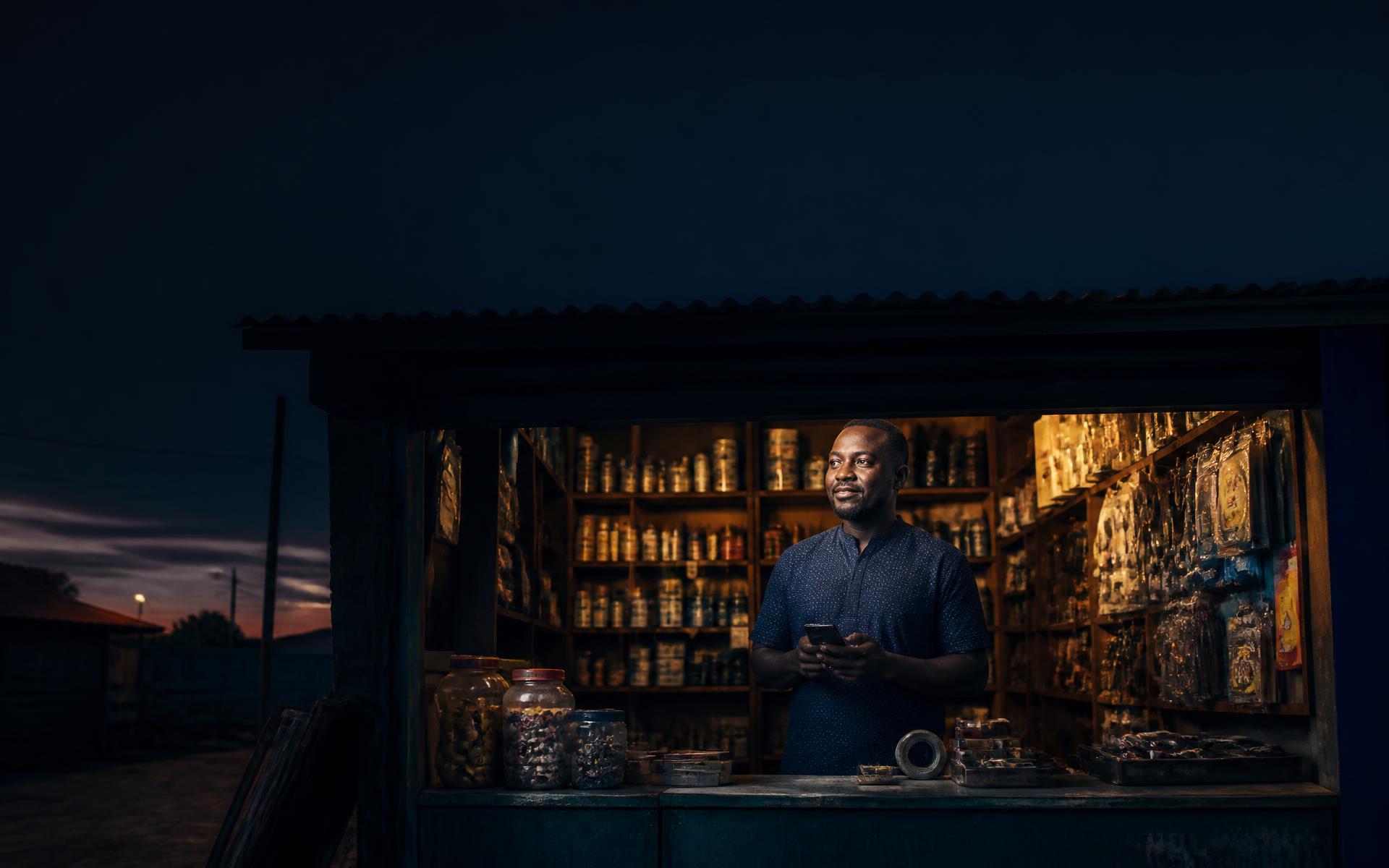 Shop owner using Kwikbooks on a phone behind the counter at dusk